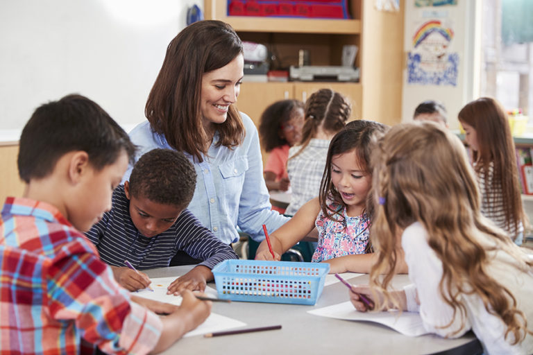 Teacher sitting at table with young school kids in lesson